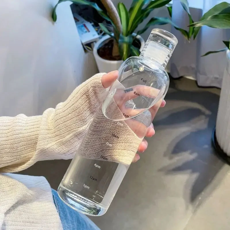 Hand holding a clear Vexo bottle with time markers, indoor setting, potted plants visible