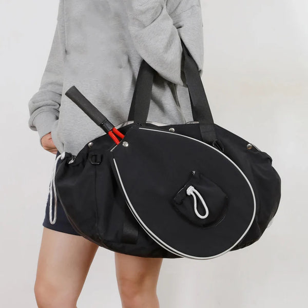 Person carrying Vexo black tennis racket bag with shoulder straps and white trim